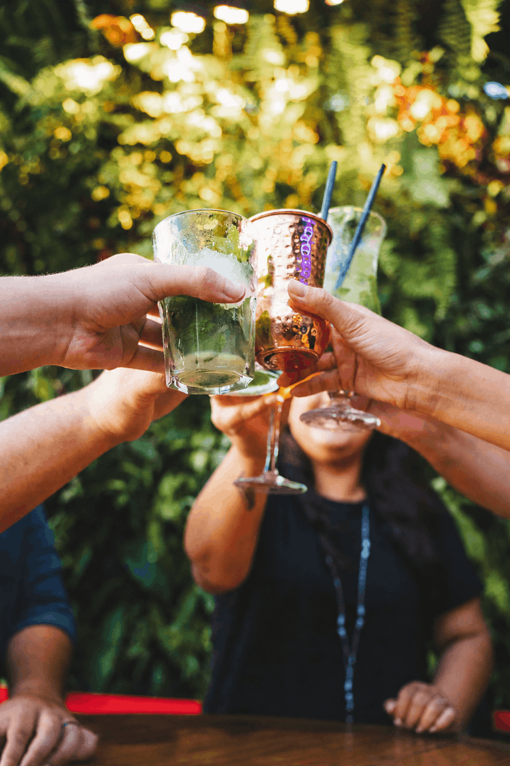Coulée de plusieurs verres de cocktails lors d'un toast dans un décor de verdure tropicale
