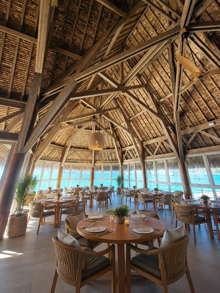 Grand pavillon de restaurant sur pilotis avec toit de chaume au-dessus du lagon, passerelle en bois