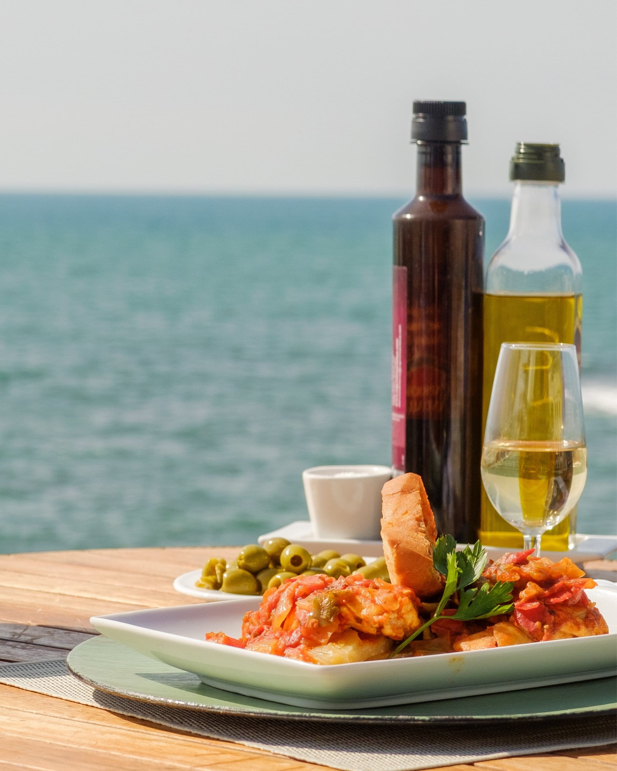 Plat mijoté sur une terrasse bois donnant sur la mer turquoise, huile et vin blanc à côté