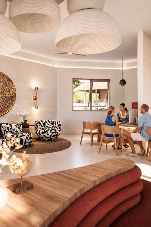 Hall d’hôtel contemporain avec réception en bois clair, personnel souriant accueillant un couple près du décor sculptural et de fauteuils au contraste monochrome.