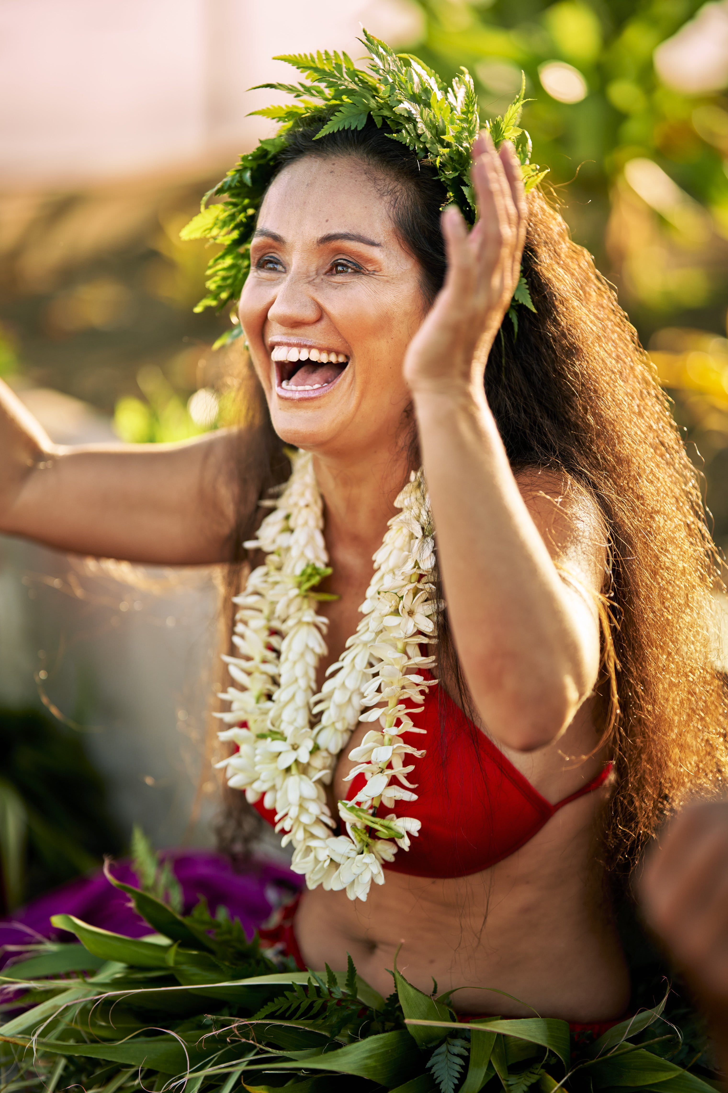 Femme souriante en tenue polynésienne traditionnelle avec collier de fleurs blanches et couronne de feuilles.