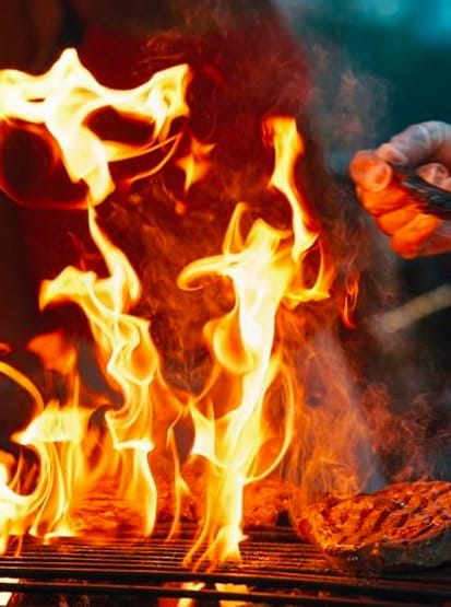 Viande grillée sur de vives flammes, main du chef avec des pinces.