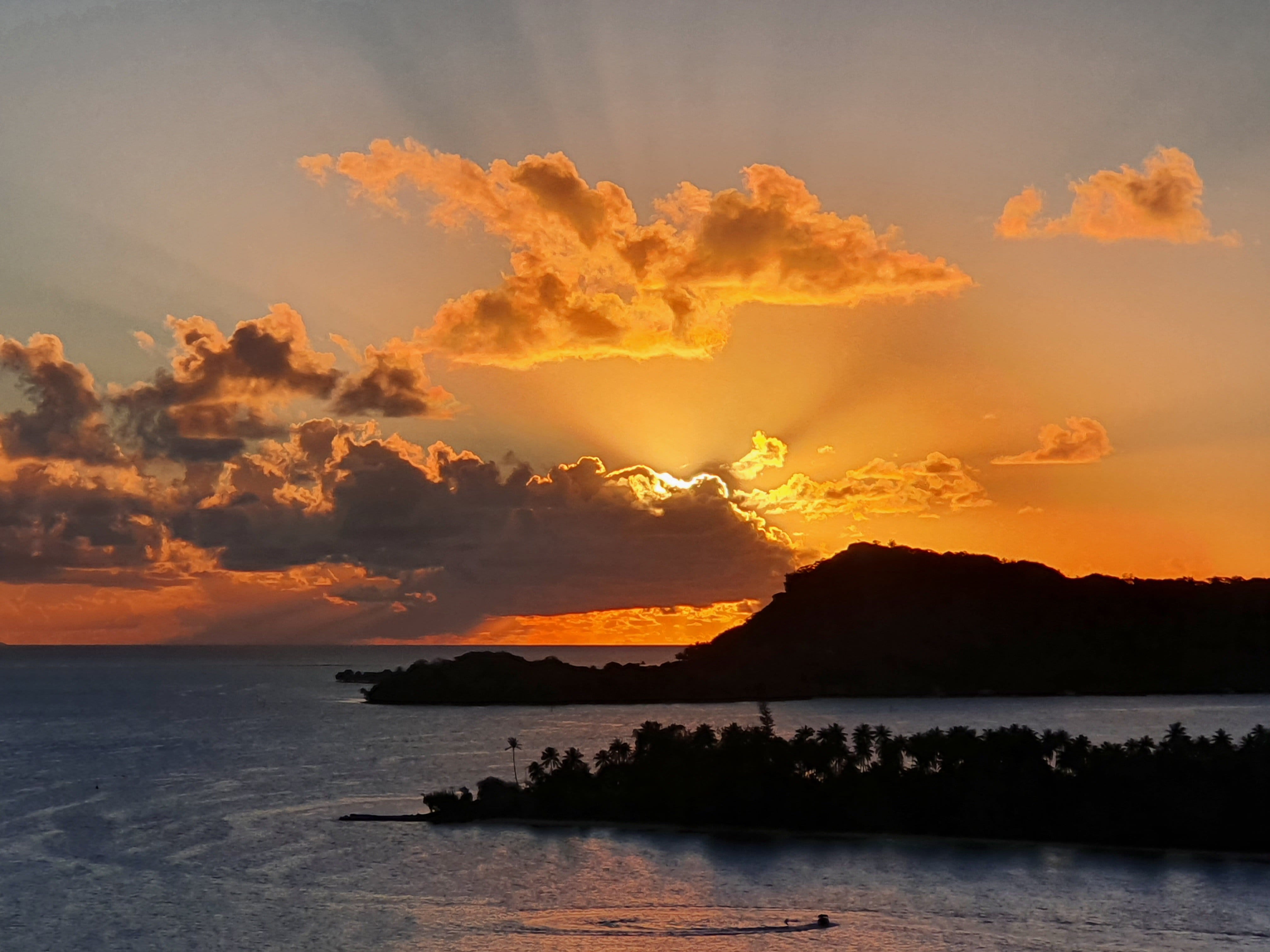 Coucher de soleil spectaculaire sur des îlots et cocotiers en silhouette, rayons de soleil à travers les nuages sur le lagon.