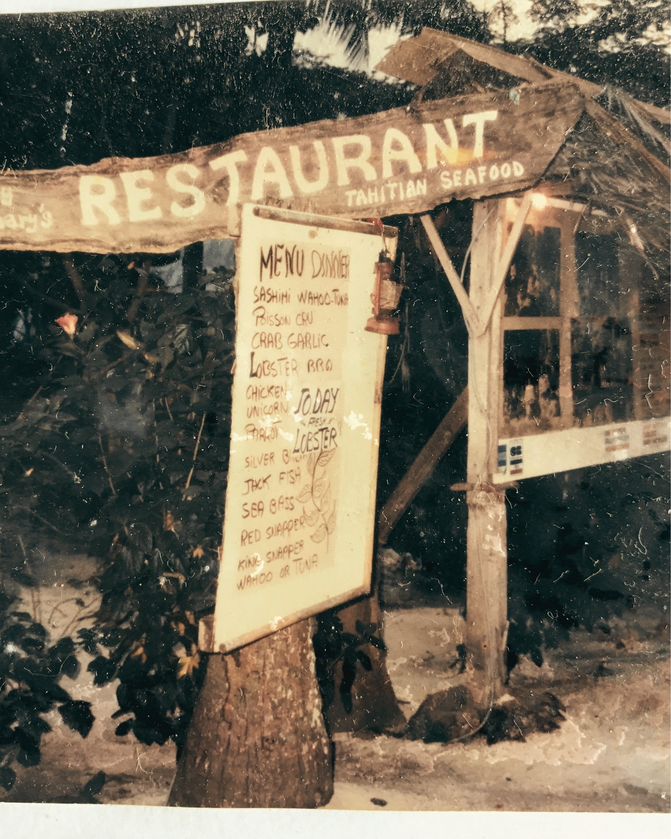 Sand path leading toward Bloody Mary's entrance flanked by a carved wooden tiki and hand-painted signage reading Since 1979